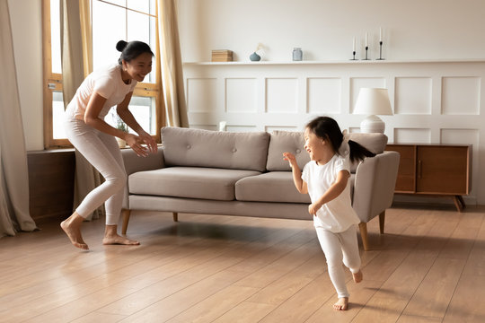 Overjoyed ethnic mother and daughter running playing at home