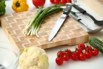 Knife and green onions for salad or fresh vegetable soup with vitamins are on wooden cutting board. Raw food and vegetarian food recipe book in modern society is a popular concept.
