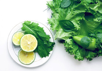 Obraz premium Detox green food. Three slices of lime on a white plate. Leaves of salad, leaves of basil, dill and green peppers.