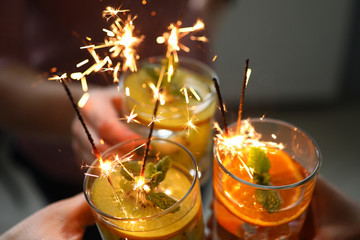 Close-up of friends hands holding three bright delicious cocktails with sparklers. Fruit alcoholic...