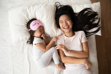 Happy Asian mom and little daughter relax in cozy bedroom