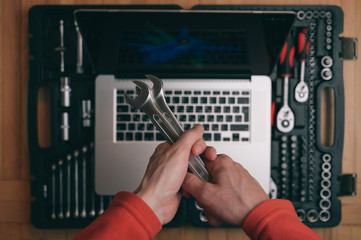 computer maintenance repair concept of man technician holding chrome socket wrench spanner on background with silver laptop on auto toolbox kit in workshop