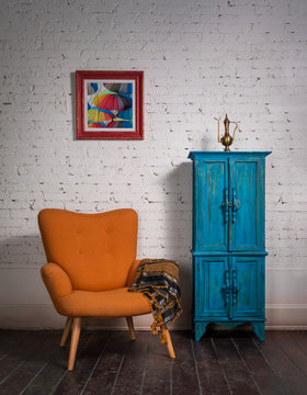 Vintage orange armchair, ornate scarf, and blue cupboard on grunge parquet floor and bricks wall