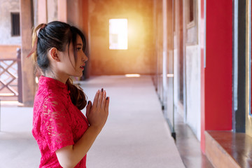 Charming young woman wear red cheongsam sitting praying pay respect to buddha statue in Chinese new year.