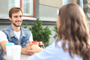 Smiling young girl having a date with her boyfriend at the coffee shop, man holding present box.