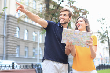 Naklejka premium Beautiful young couple holding a map and smiling while standing outdoors.
