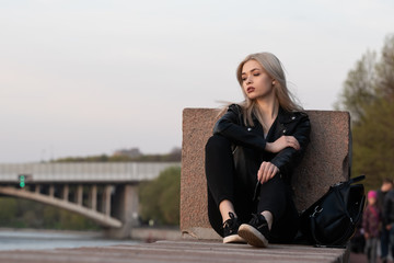 Young fashion blond woman in leather jacket with handbag on city street