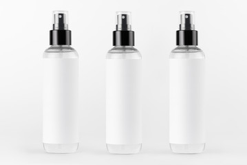 Tall transparent spray dispenser bottles for cosmetics product collection in a row with white label on white background, mock up for design.