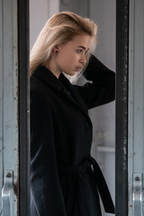 A young beautiful blonde girl in a black coat poses in the doorway of an electric train