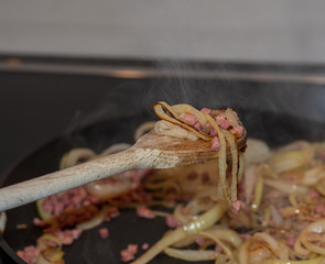 Zwiebelringe und Schinken in Bratpfanne anbraten
