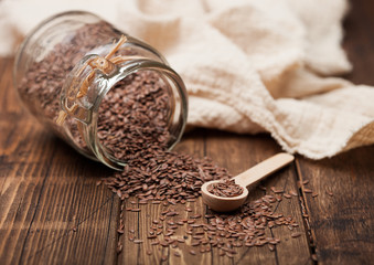 Glass jar of raw natural organic linseed flax-seed with spoon and linen cloth on wooden background.