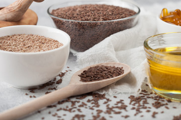 Bowl of raw natural organic linseed flax-seed with spoon and oil on light table background with linen cloth.