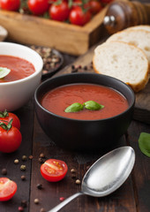 Ceramic bowl plates of creamy tomato soup with spoon, pepper and kitchen cloth on wooden background with box of raw tomatoes and bread.