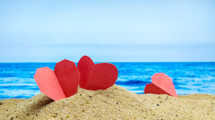 Focus on the red paper hearts on the sandy beach, blur the sea view and the sky as a backdrop.