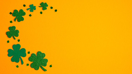 St Patricks Day frame border of shamrock and four-leaf clovers on orange background. Flat lay, top...