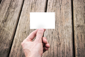 hand holding a blank business card, wooden texture on background