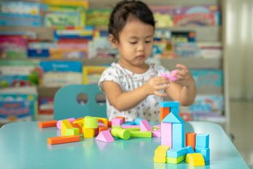 Fototapeta premium Cute little girl playing with multicolor wooden building blocks on blue table.