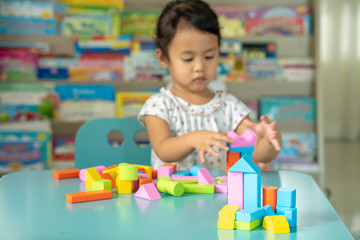 Fototapeta na wymiar Cute little girl playing with multicolor wooden building blocks on blue table.