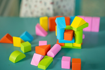 Cute little girl playing with multicolor wooden building blocks on blue table.