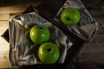 Still life of fruit, with 3 green apples on a wooden tray. Closeup and depth of field