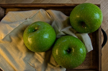 Still life of fruit, with 3 green apples on a wooden tray. Closeup and depth of field