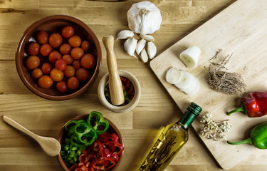 Fresh vegetable ingredients, with kitchen utensils, bottle of oil, all on a wooden board