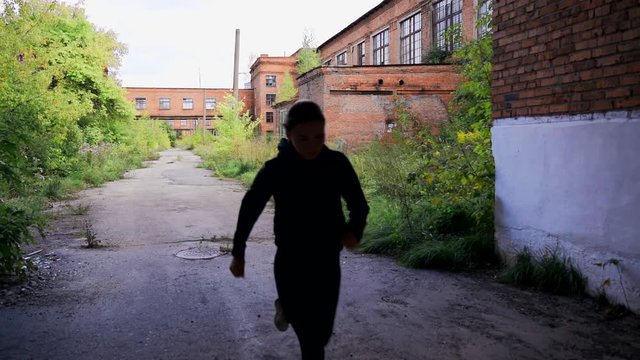 The girl in a black tracksuit runs through the territory of an abandoned factory.