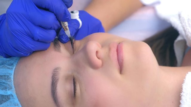 Premanent eyeliner on eyelids for young woman in beauty clinic, closeup face, side view. Cosmetologist making beauty procedure for young woman in clinic, hands closeup.