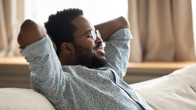 Happy african guy relaxing on couch eyes closed breathing air