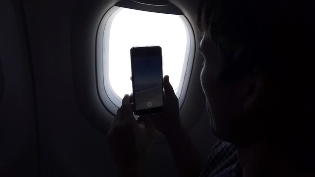 Young man takes a picture on the phone of a view from the airplane window in flight