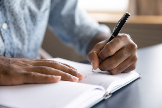 Close Up View Of African Left-handed Businessman Writing In Notebook