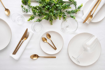 Tableware background in white gold tone.White plates,  gold cutlery,  wine glasses and decorative...