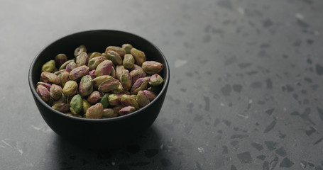 peeled pistachios in black bowl on terrazzo surface