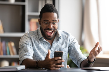 Overjoyed african business man using smartphone excited about mobile win
