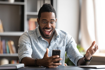 Overjoyed african business man using smartphone excited about mobile win