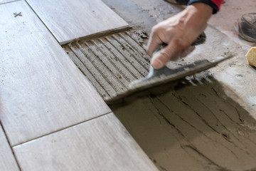 Man installing rectangular shaped floor tiles in kitchen. Applying adhesive before installation and verifying afterwards