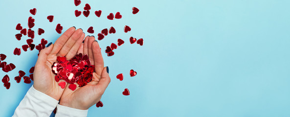 Obraz na płótnie Canvas Female hands holding red sparkling heart-shaped confetti over blue background
