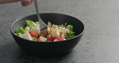 man hand pick salad with mozzarella, cherry tomatoes and frisee leaves in black bowl on terrazzo surface