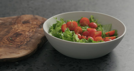 preparing salad with mozzarella, cherry tomatoes and frisee leaves in white bowl on terrazzo surface