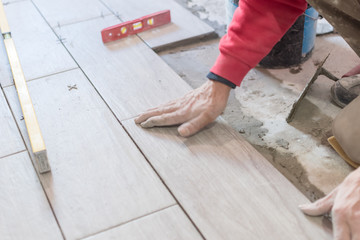 Man installing rectangular shaped floor tiles in kitchen. Applying adhesive before installation and verifying afterwards