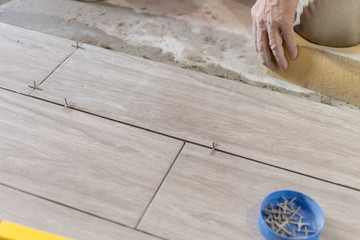 Man installing rectangular shaped floor tiles in kitchen. Applying adhesive before installation and verifying afterwards