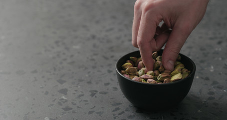 man hand takes pistachio kernels from black bowl on terrazzo surface