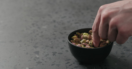 man hand takes pistachio kernels from black bowl on terrazzo surface