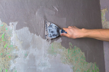 Plaster the wall with a putty knife.Internal construction and finishing works.The Builder puts plaster on the wall.Hand holding a spatula with construction mix and smoothes out bumps.Repair the wall