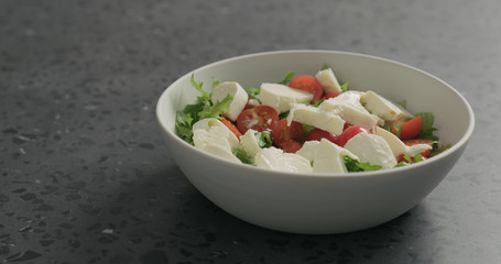 salting salad with mozzarella, cherry tomatoes and frisee leaves in white bowl on terrazzo surface