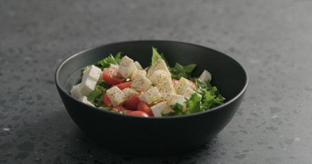 ground spices to salad with mozzarella, cherry tomatoes and frisee leaves in black bowl on terrazzo surface