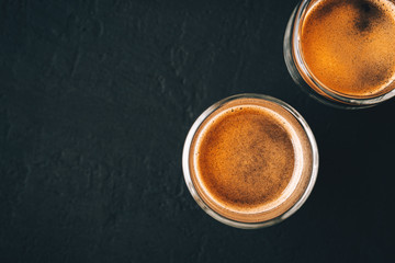 Two shots of espresso in glass transparent cups on a dark stone background,top view,copy space
