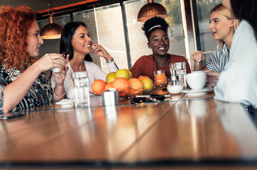 Group of young female friends having fun in cafe talking and laughing while sitting at table.	