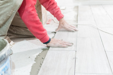 Man installing rectangular shaped floor tiles in kitchen. Applying adhesive before installation and verifying afterwards