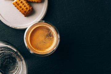 One portion of espresso in glass transparent cups,bisuits and water on a dark stone background,copy space